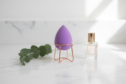 Clean girl aesthetic lifestyle flat lay with lavender makeup blender on rose gold stand on marble